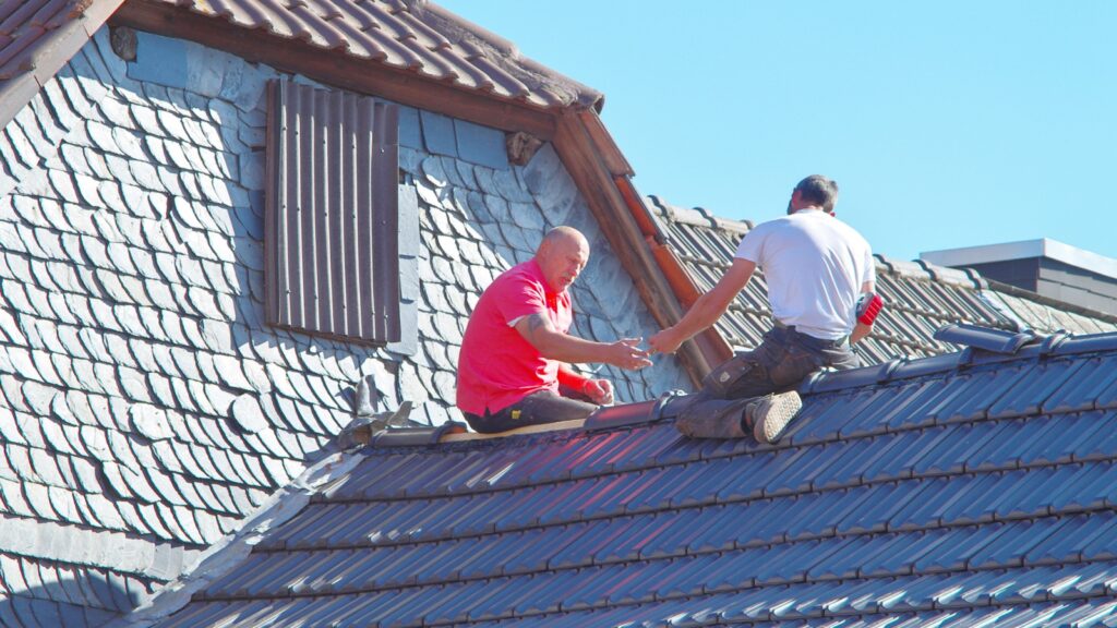 two roofers passing an interlocking tile along a laid course